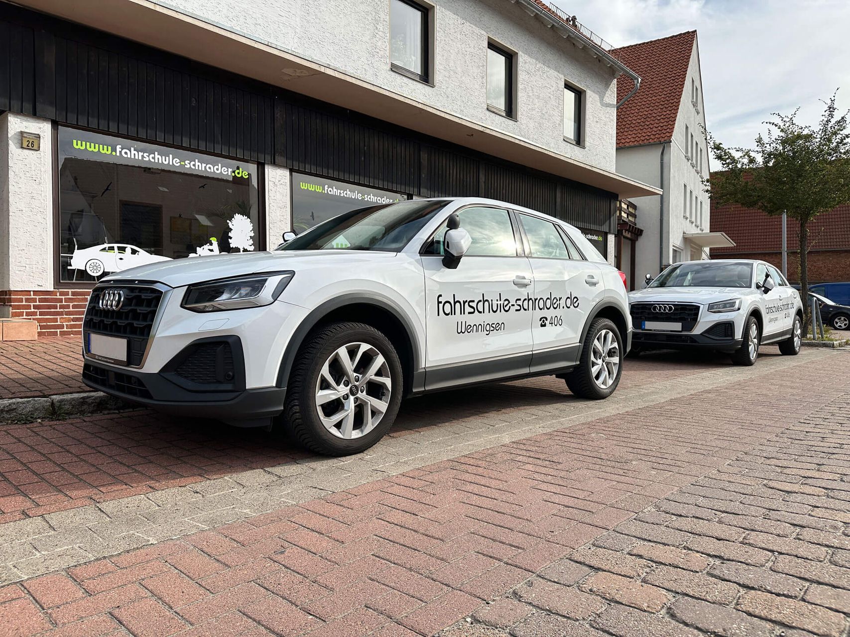 Weiße Fahrschulautos, die vor einem Gebäude mit Beschilderung geparkt sind.