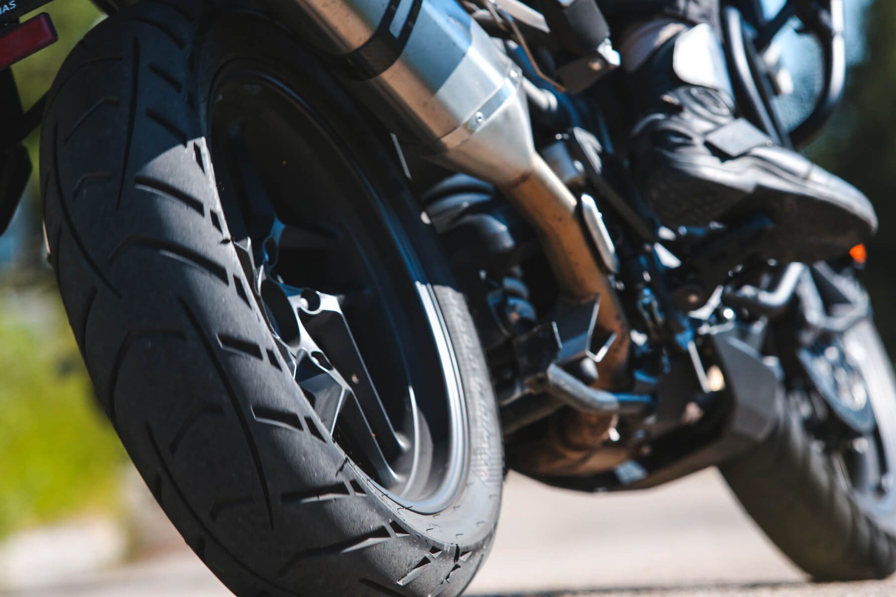 Nahaufnahme des Hinterrads eines Motorrads, des Auspuffs und eines Teils des Motors.
